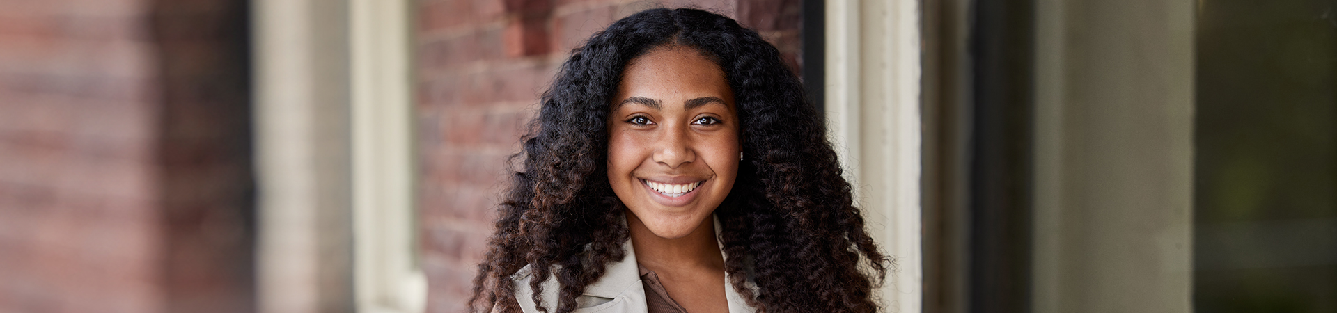  portrait of ambassador girl scout wearing vest and smiling at camera in front of a brick building 